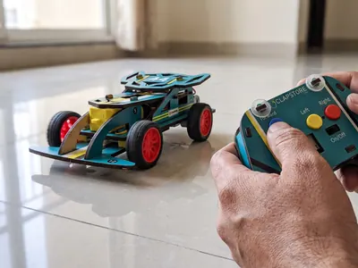 The built car on a tiled floor with the remote in an adult's hand
